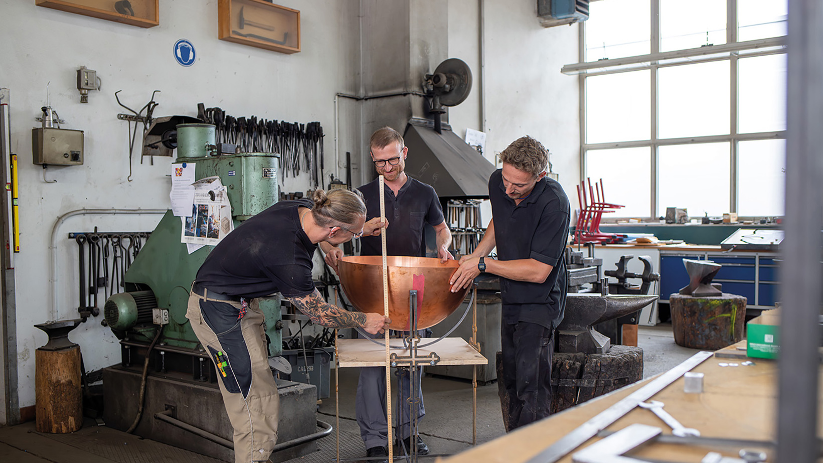 Drei junge Handwerker beim Ausmessen einer Kupferhalbkugel