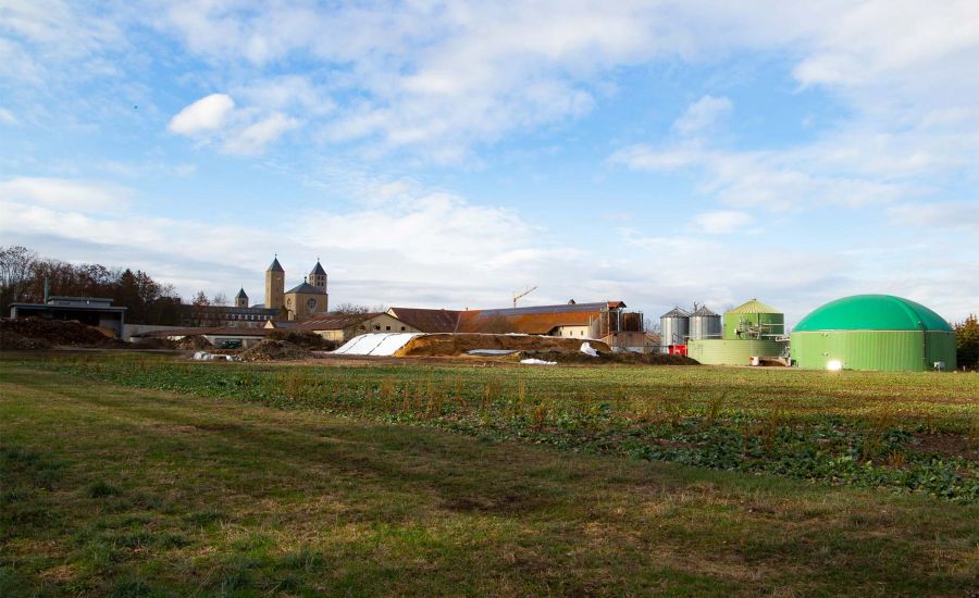 Blick auf eine Biogasanlage, im Hintergrund die Türme einer Kirche