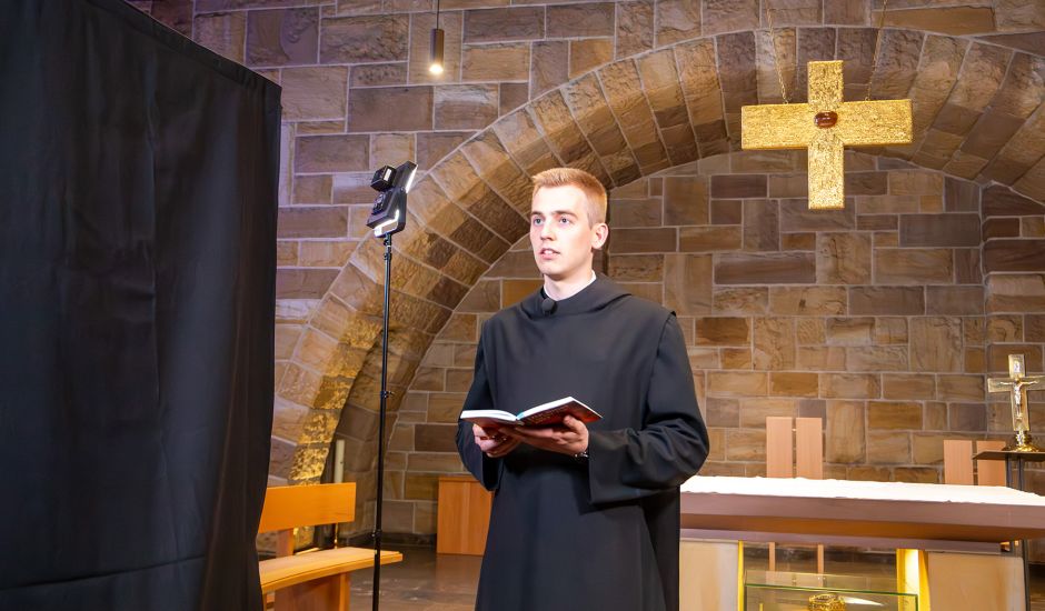 Junger Mönch mit Buch in der Hand vor einem Tischaltar