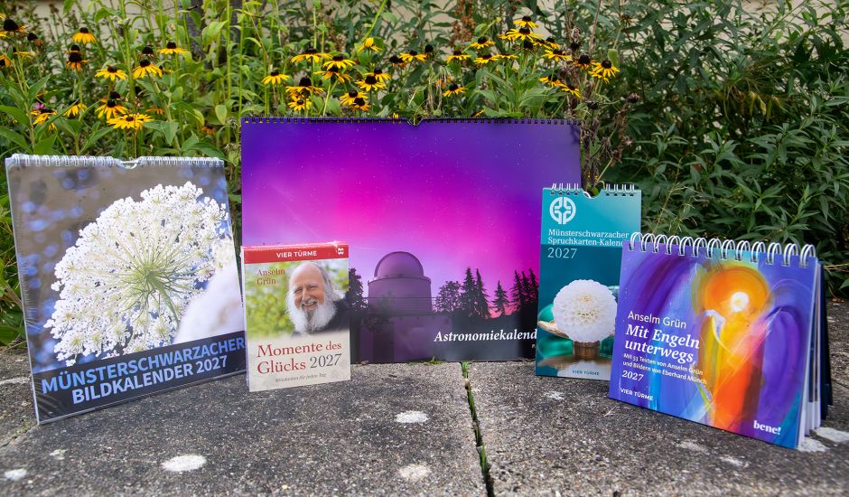 Fünf Kalender für 2027 auf einer Betonfläche, daher sind gelbblühende Blumen