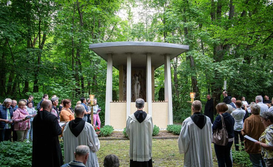 Gruppe von Menschen steht vor einer Marienkapelle in einem Park