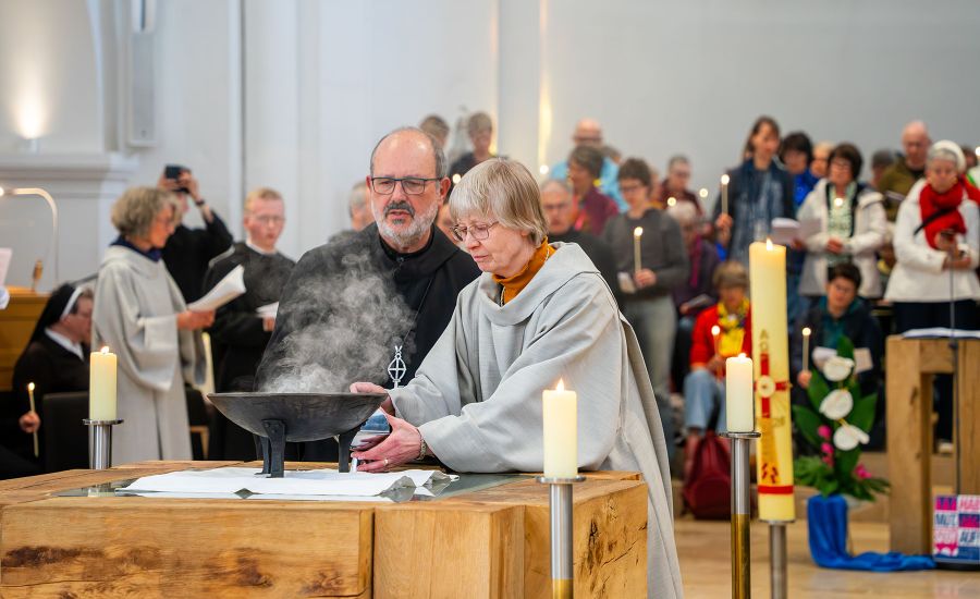 Mönch und Schwester vor rauchendem Behältnis am Altar