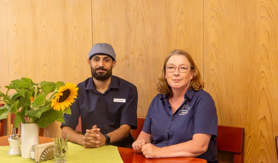 Azubi Saad und Ausbildungsleiterin Anja sitzen an einem Tisch mit Sonnenblumenstrauß
